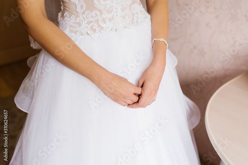 Bride's hands on the background of her white wedding dress
