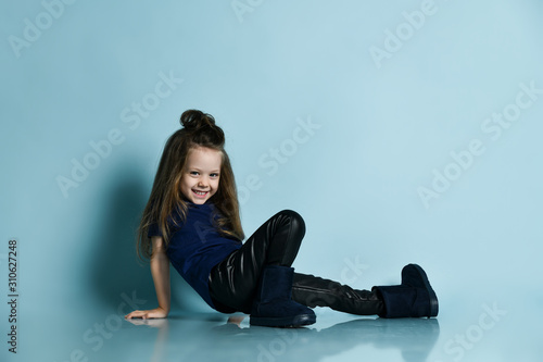 Small smiling cute girl in t-shirt, leather leggins and dark blue ugg boots posing on floor