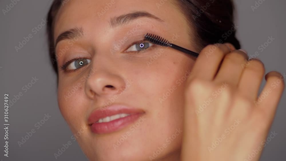 beauty, makeup and cosmetics concept - face of beautiful young woman applying mascara over grey background beauty, makeup and cosmetics concept - face of beautiful young woman applying mascara over grey background