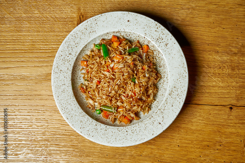 Rice with vegetables on a white plate on a wooden background. Vegetarian food. Dietary and healthy nutrition. Top view