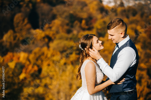 Lovely young couple in wedding clothes standing on a hill on city background