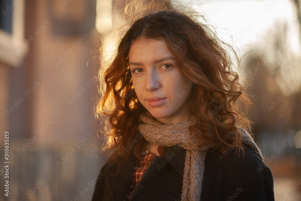 Dreaming young woman with spectacular curly red ginger hair looking at camera posing outdoor in downtown street. Female portrait. Dreaming young woman with spectacular curly red ginger hair looking at camera posing outdoor in downtown street. Female portrait.