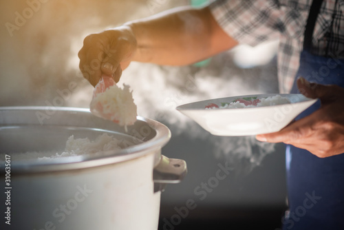 Tableau sur toile The mass of steam reflected in the morning light coming out of a large electric rice cooker that is heated in the cafeteria, where the cook is scooping the rice onto a dish