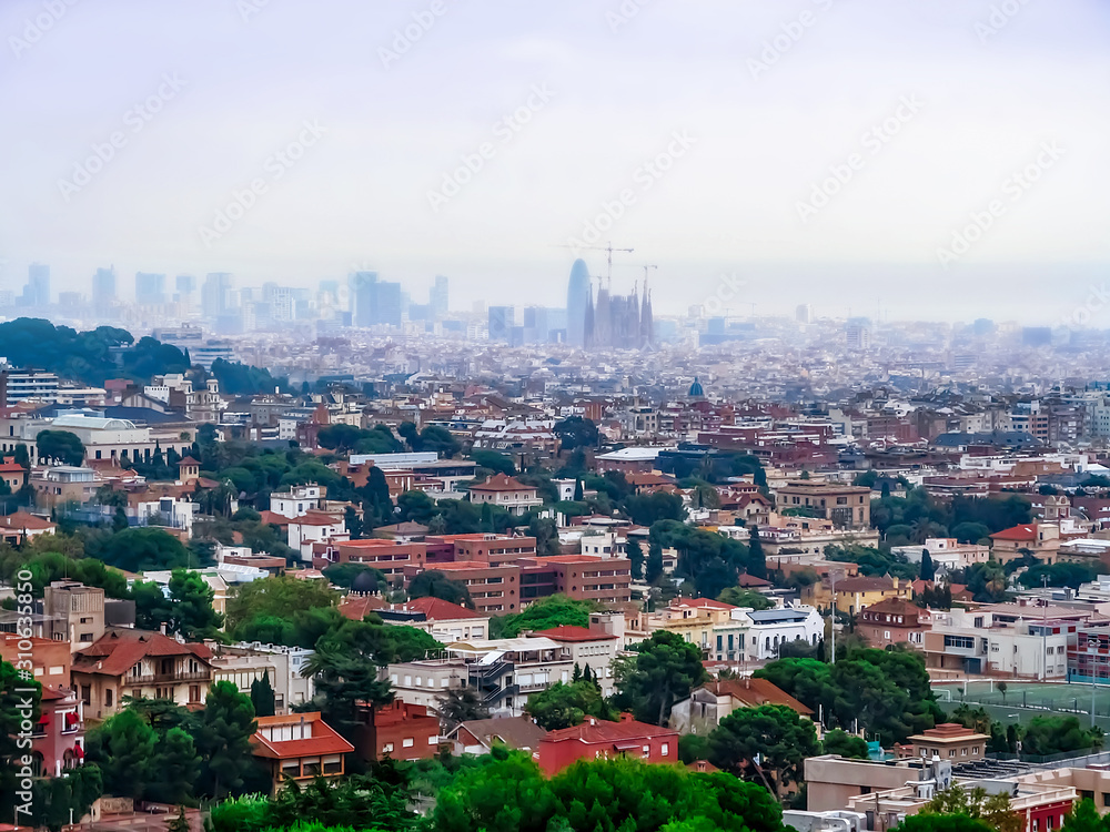 Beautiful panorama of Barcelona with the silhouette of the Basilica de la Sagrada Familia on the horizon in fog. European city landscape with dense construction of old houses, aerial view, close-up