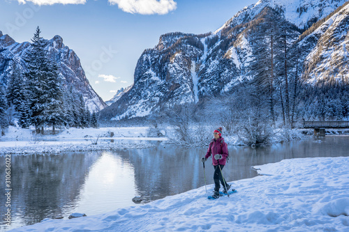 nice senior woman snowshoeing on a cold winter morning on the shore of Lago Dobbiaco, Three Peak Dolomites, South Tyrol, Italy