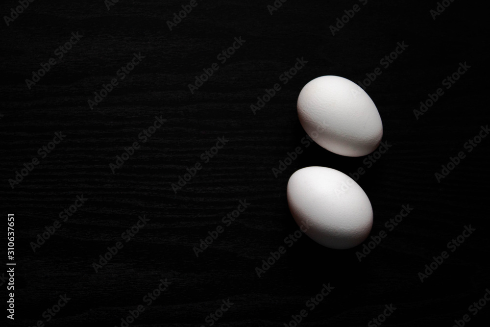 Two white chicken eggs on a black background close up Two white chicken eggs on a black background close up