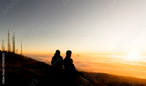 Silhouette of two friends man standing on a rock at sunrise on the fog of success and serenity.