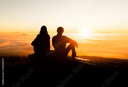 Silhouette of two friends man standing on a rock at sunrise on the fog of success and serenity.