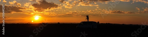 Panoramic of a field sunset with photographer taking pictures on top of the van