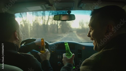 Scene of two men ride in a car with bottles of alcohol, they drink alcohol while driving, chatting, laughing. The camera is behind. Drunk driver idea and concept