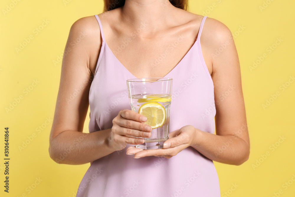 Young woman with glass of lemon water on yellow background, closeup Young woman with glass of lemon water on yellow background, closeup
