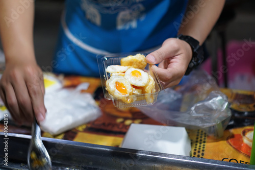 The seller scooped the fried quail eggs into a plastic dish. focus quail eggs