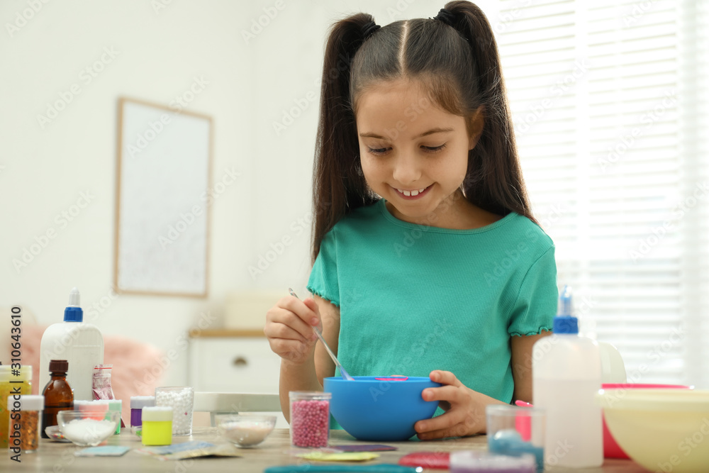 Cute little girl mixing ingredients with silicone spatula at table in room. DIY slime toy Cute little girl mixing ingredients with silicone spatula at table in room. DIY slime toy