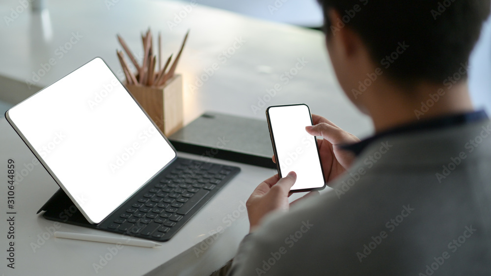 Young businessman hold a blank screen smartphone in hand and a blank screen laptop on the desk. Young businessman hold a blank screen smartphone in hand and a blank screen laptop on the desk.