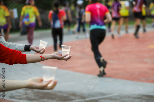 Hand of a volunteer giving a cup of water at a refreshment point in a marathon race to runners., selective focus