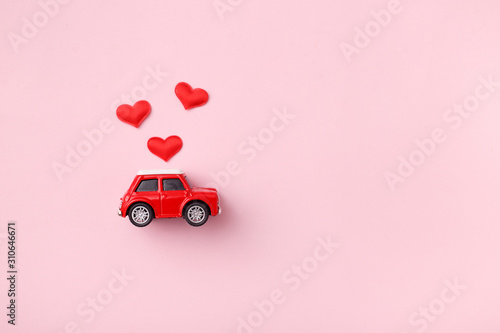 Red retro toy red car with red bow for Valentine's day on pink background with heart confetti. Top view, flat lay photo