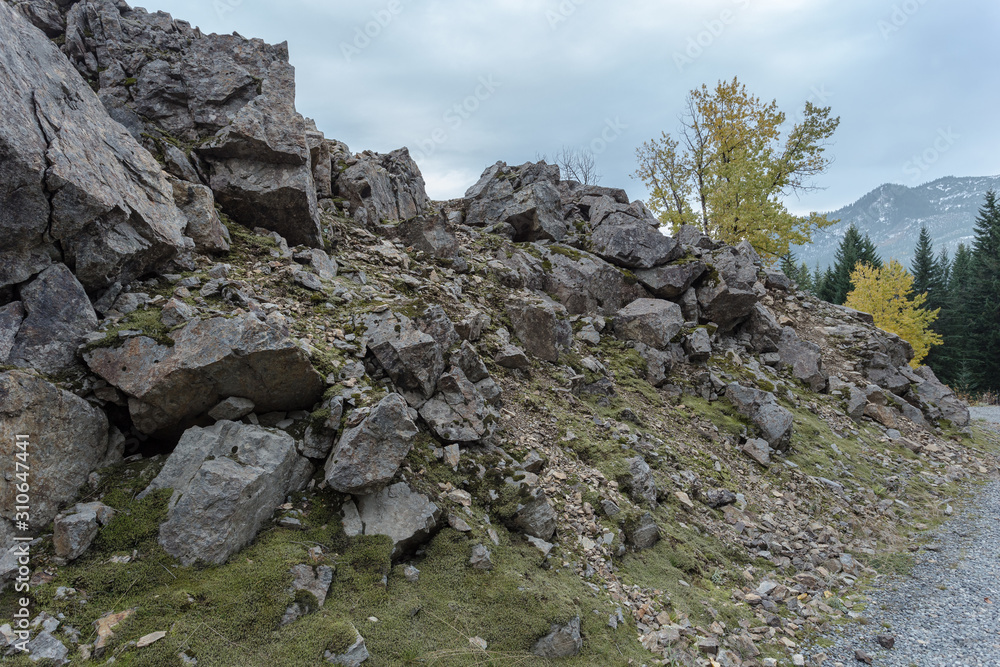 Harsh rock formations creating rough hill next to gravel road with fall colors