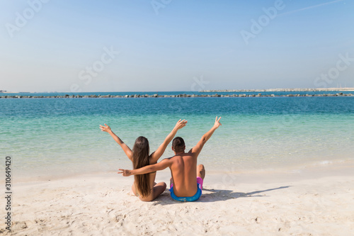 Young couple sitting on a tropical sandy beach  Rear view.
