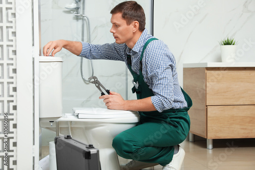 Professional plumber repairing toilet tank in bathroom