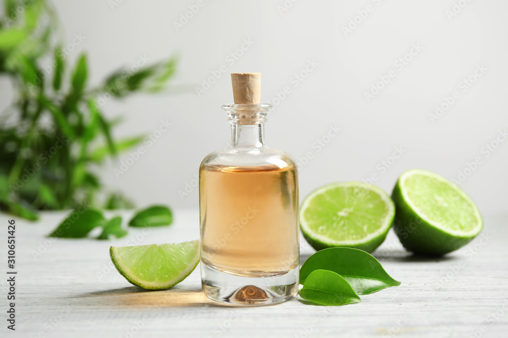 Lime essential oil and cut citrus fruits on white wooden table Lime essential oil and cut citrus fruits on white wooden table