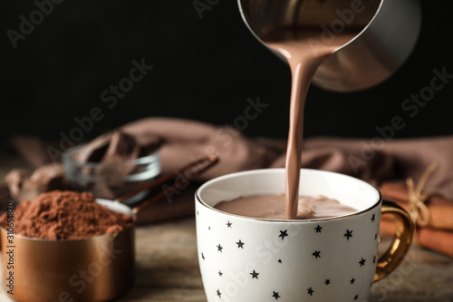 Pouring hot cocoa drink into cup on wooden table