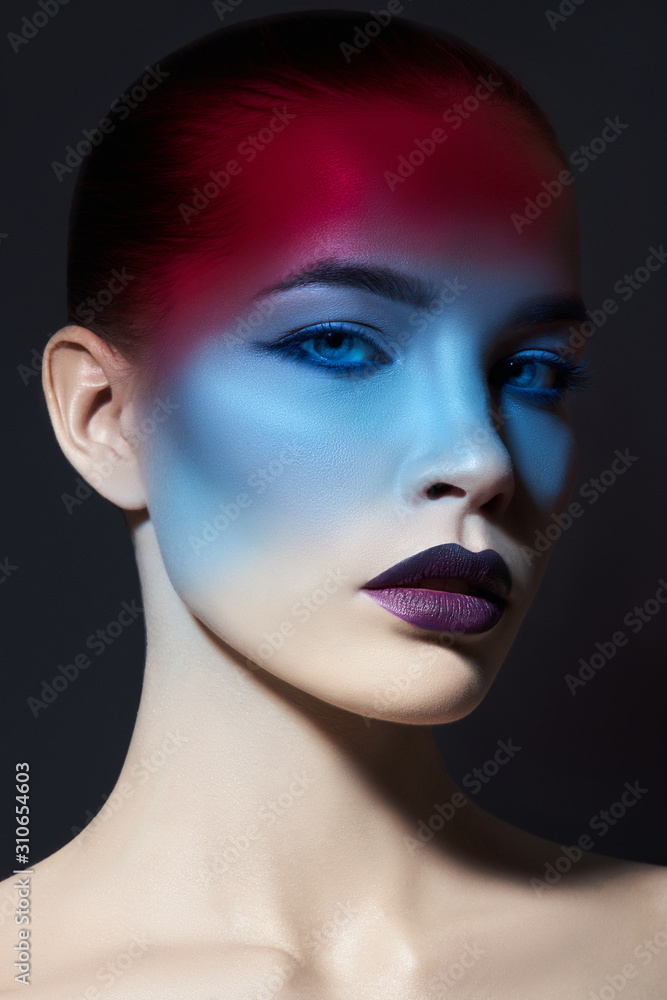 Bright contrasting beauty makeup portrait of a woman in blue and red shadow tones. Perfect clean skin and face makeup, dark lipstick on plump lips Bright contrasting beauty makeup portrait of a woman in blue and red shadow tones. Perfect clean skin and face makeup, dark lipstick on plump lips