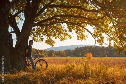 young man with a bicycle at the tree. autumn landscape.