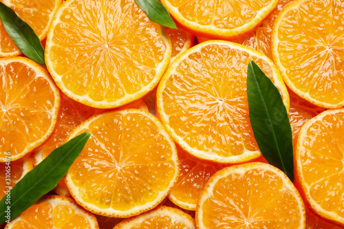 Slices of fresh ripe tangerines and leaves as background  top view. Citrus fruit