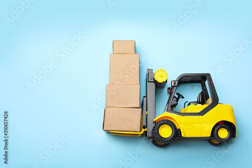 Top view of toy forklift with boxes on blue background, space for text. Logistics and wholesale concept