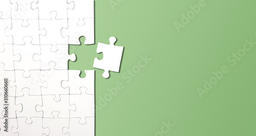 top view of jigsaw puzzle with one piece left on green background, completing a task or solving a problem concept