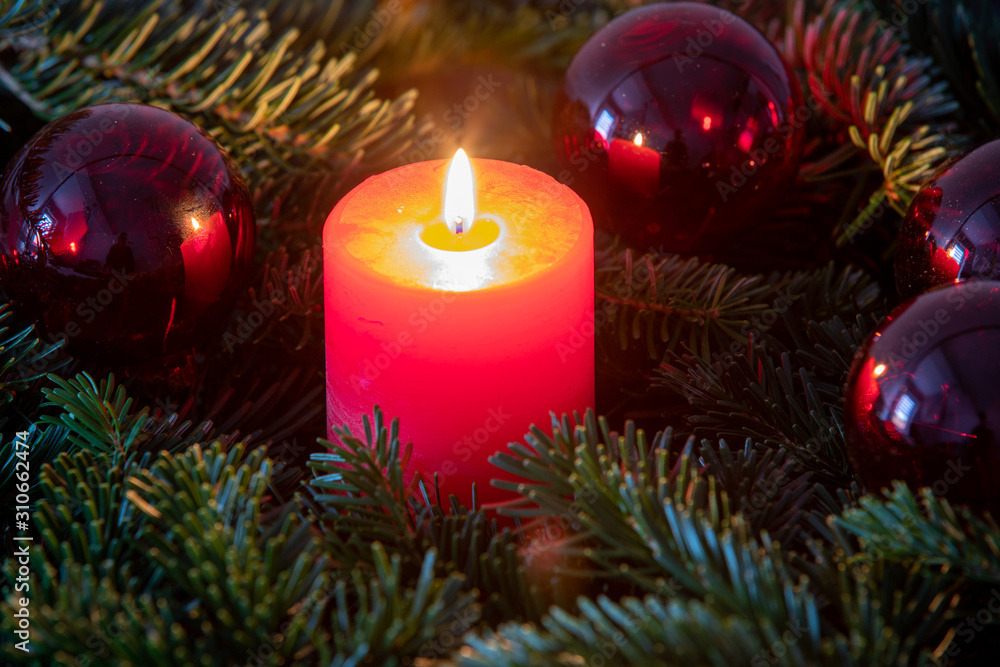 Christmas motif with red burning candle surrounded by Nordmann fir branches, red christmas tree balls and gift parcel Christmas motif with red burning candle surrounded by Nordmann fir branches, red christmas tree balls and gift parcel