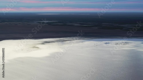 A flock of gray cranes flies over the lake at dawn, shot from a drone photo