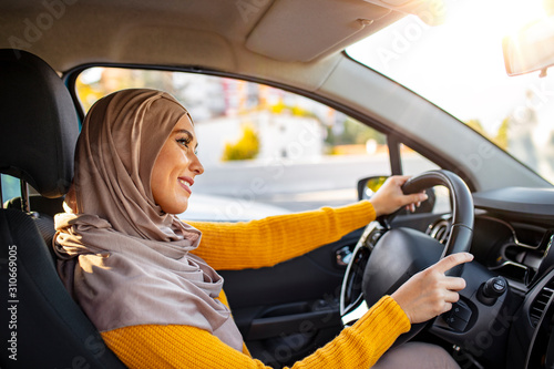 Beautiful  Muslim woman driving a car wearing hijab. Emirati woman driving a car in Dubai at sunset. Portrait of a Middle Eastern woman driving a car, she is wearing a modern beige Abaya. photo