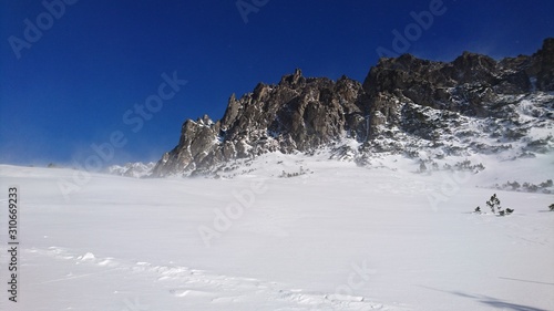Alpine winter mountains covered with thick snow. Wind blowing snow in a sunny day