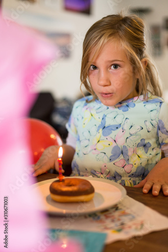 Mädchen im Kleid bläst Kerze auf Doughnut aus