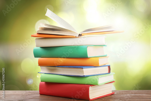 Stack of colorful books on wooden table against blurred green background