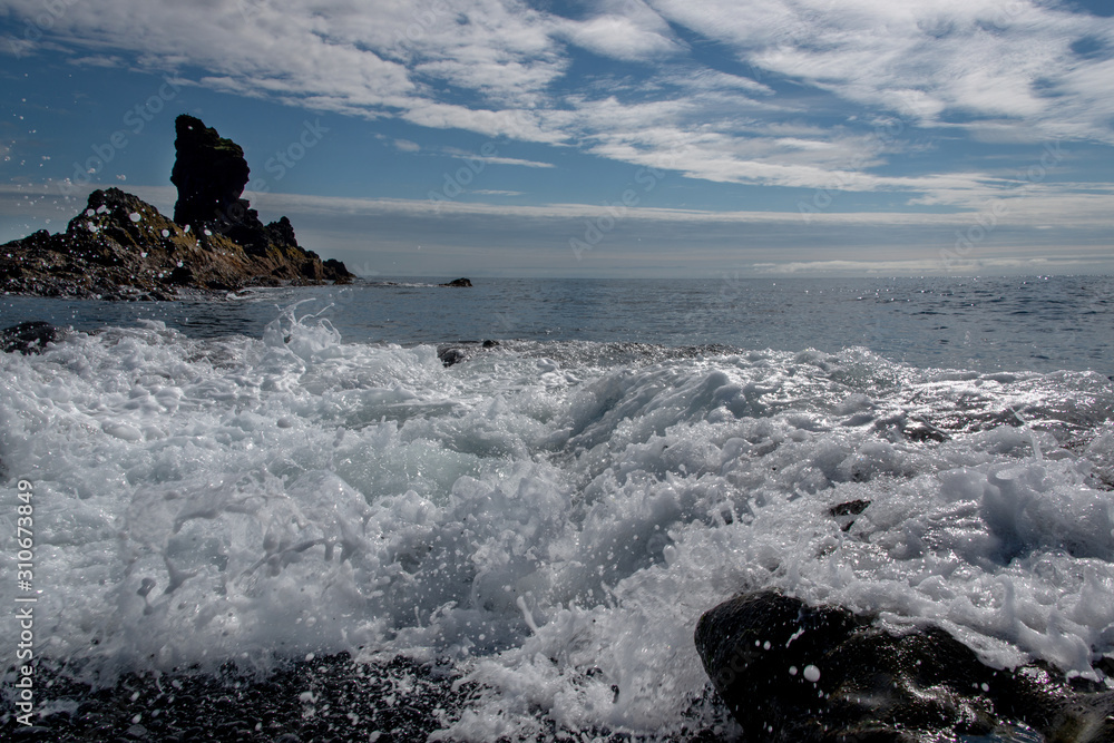 aufgewühlte Gischt am schwarzen Steinstrand auf Island im Sonnen