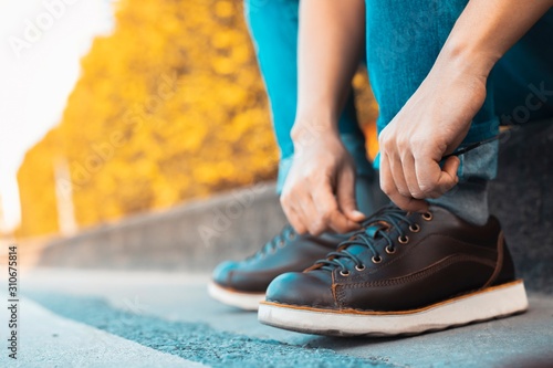 image of man is shoelace on wearing brown leather shoes 