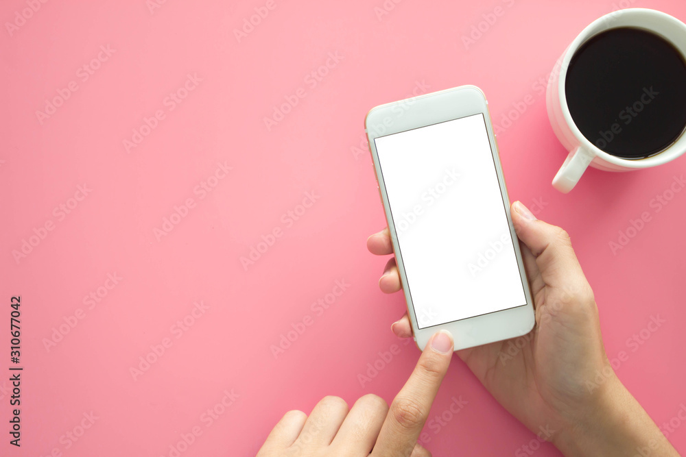 Mockup image of hands holding white mobile phone with blank white .screen with  Modern pink office desk with laptop and other supplies for input the text on copy space Top view, flat lay. - obrazy, fototapety, plakaty 