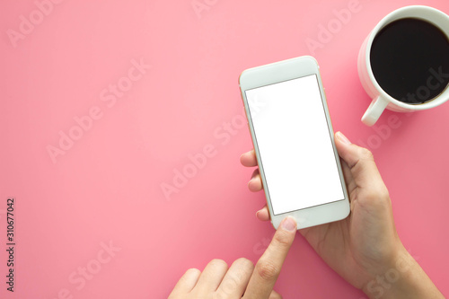 Mockup image of hands holding white mobile phone with blank white .screen with  Modern pink office desk with laptop and other supplies for input the text on copy space Top view, flat lay.