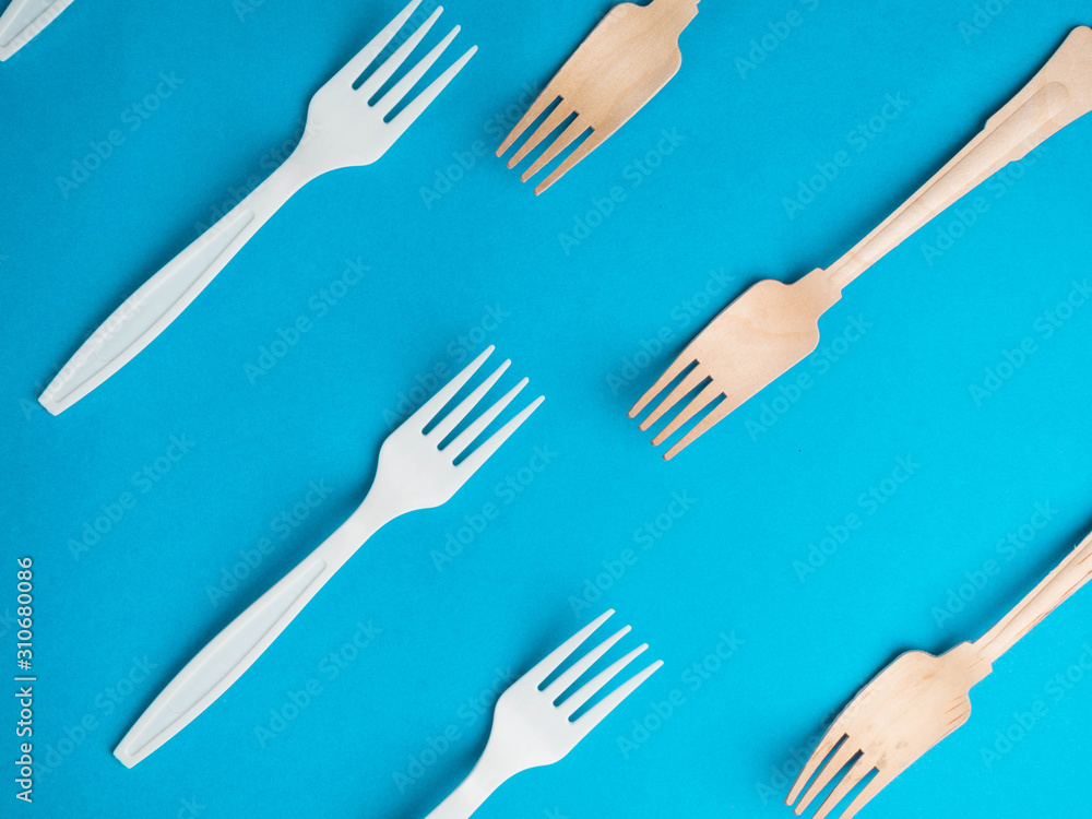 Organic bamboo disposable forks vs plastic ones on trendy blue background. Environmentally friendly wooden and non-oragnic plasticforks Organic bamboo disposable forks vs plastic ones on trendy blue background. Environmentally friendly wooden and non-oragnic plasticforks