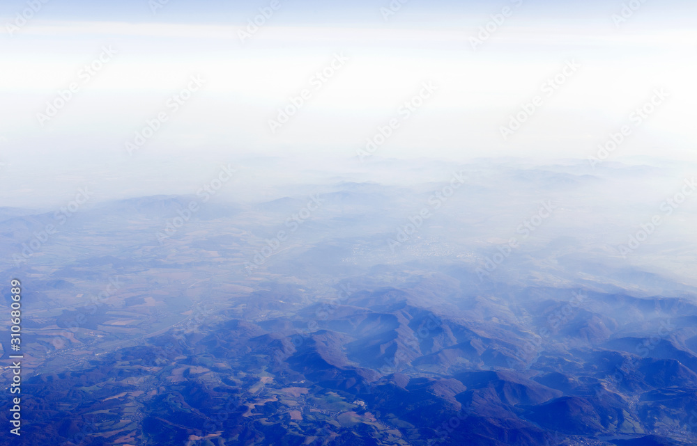 View from aircraft window at land with mountains and cloudy sky
