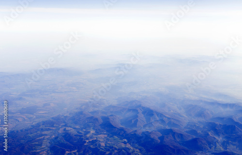 View from aircraft window at land with mountains and cloudy sky