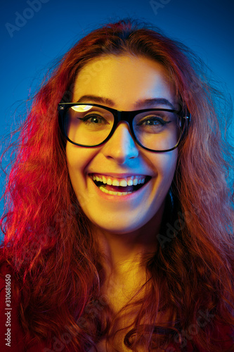 Caucasian woman's portrait isolated on blue studio background in neon light. Beautiful female model with red hair in casual style. Concept of human emotions, facial expression, sales, ad. Laughting.