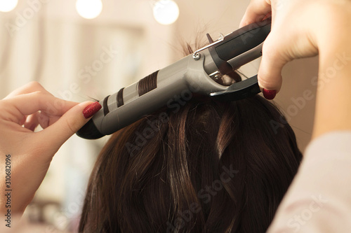 Hairstylist twists the hair of the client using a hair curler