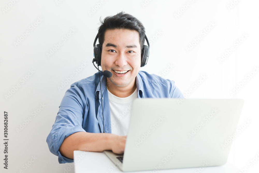 Asian handsome man in blue shirt using laptop with headphone talking smile and happy face Asian handsome man in blue shirt using laptop with headphone talking smile and happy face