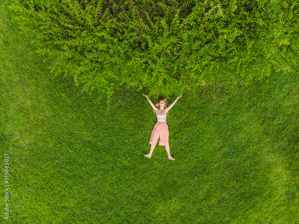 Young woman lying down in the middle of a field and relaxing, drone photo