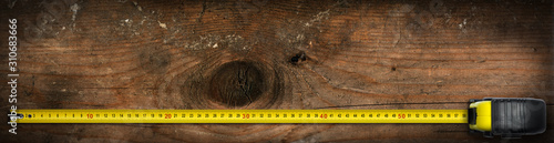 Close-up of a yellow and black tape measure on an old work table with copy space and dark shadows photo