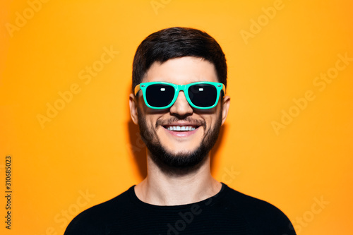 Studio portrait of young smiling hipster with aqua menthe sunglasses on orange background. © Lalandrew
