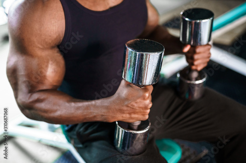 African male athlete doing exercises with dumbbells while sitting on a bench in the gym